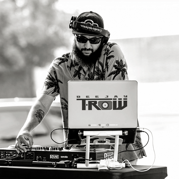 DJ T-ROW derrière sa console de musique avec une casquette et des lunette de soleil
